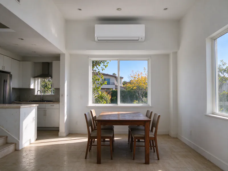 White wall-mounted mini split head above a window in the open kitchen and dining area of a San Diego house